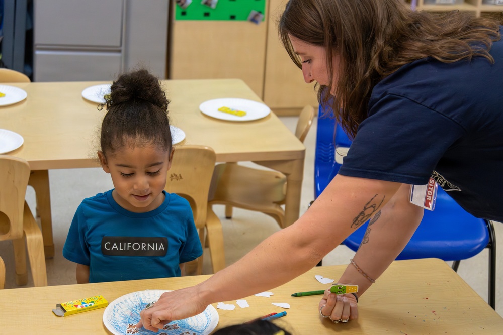 Liz Barron assists child during Earth Day event aboard Child development Center