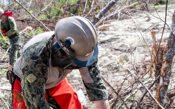 NMCB 1 Sailors clear an area with chainsaws and a backhoe