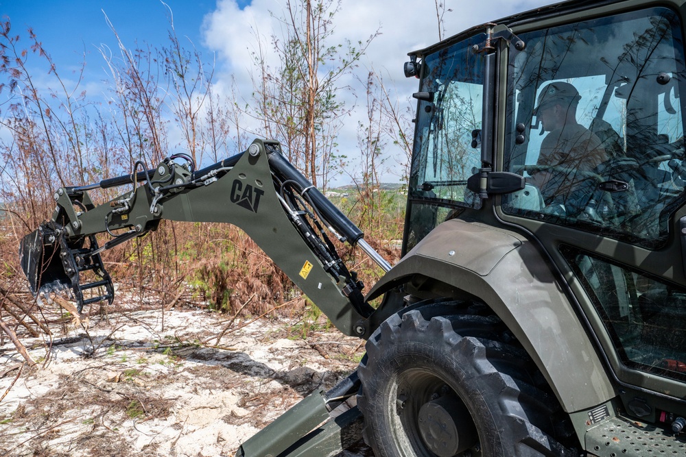 NMCB 1 Sailors clear an area with chainsaws and a backhoe