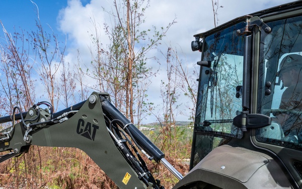 NMCB 1 Sailors clear an area with chainsaws and a backhoe