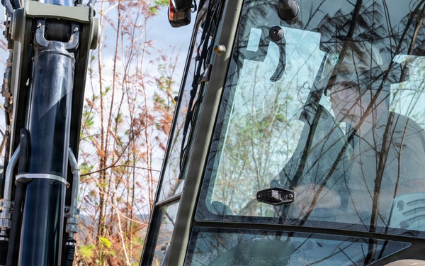 NMCB 1 Sailors clear an area with chainsaws and a backhoe