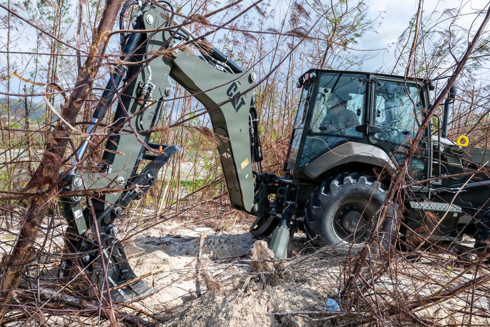 NMCB 1 Sailors clear an area with chainsaws and a backhoe