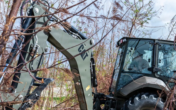 NMCB 1 Sailors clear an area with chainsaws and a backhoe