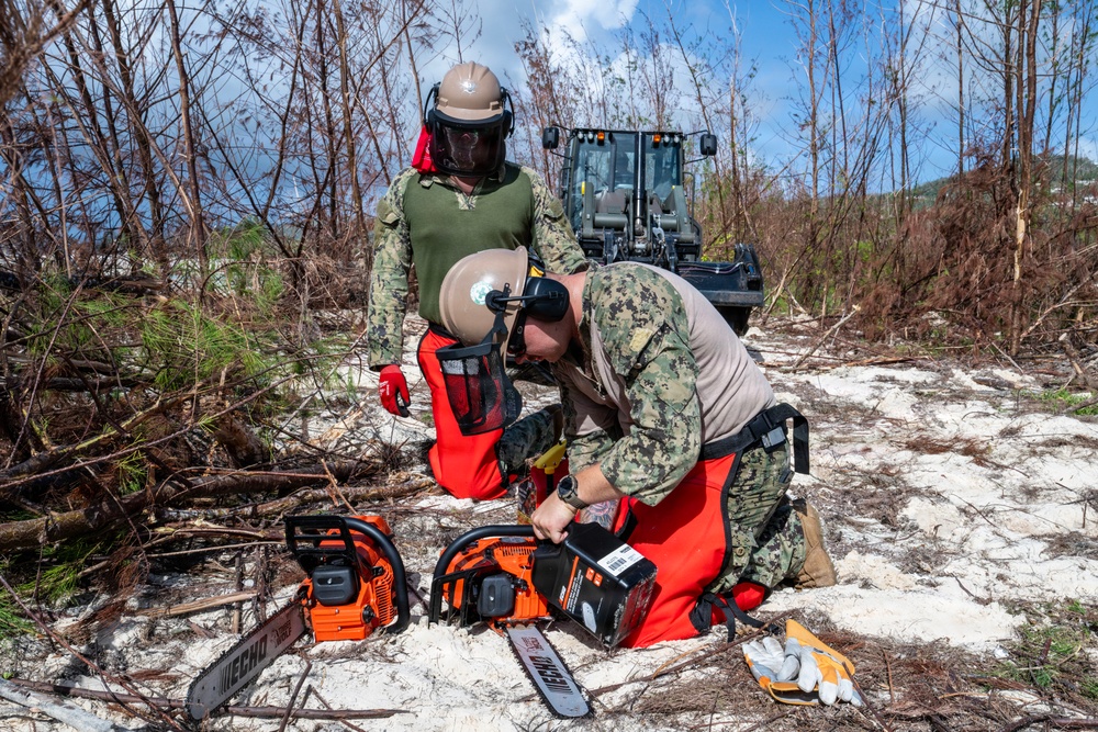 NMCB 1 Sailors clear an area with chainsaws and a backhoe