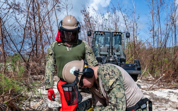 NMCB 1 Sailors clear an area with chainsaws and a backhoe