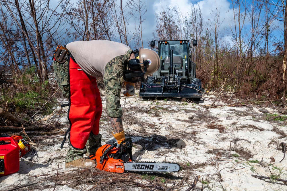 NMCB 1 Sailors clear an area with chainsaws and a backhoe