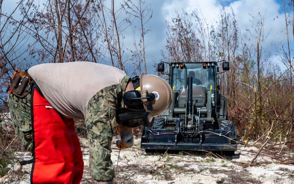 NMCB 1 Sailors clear an area with chainsaws and a backhoe