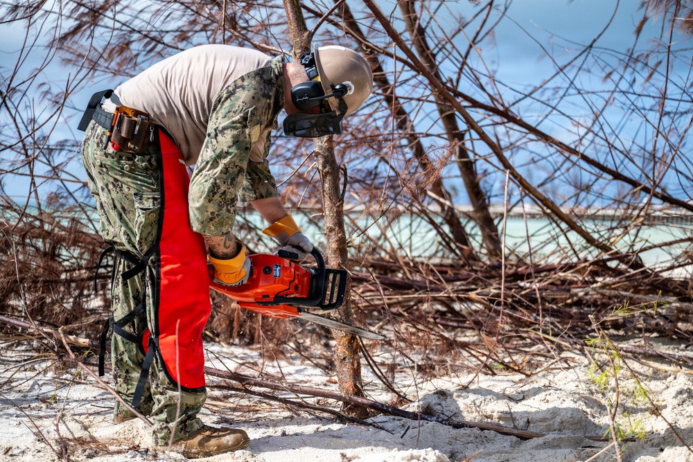 NMCB 1 Sailors clear an area with chainsaws and a backhoe