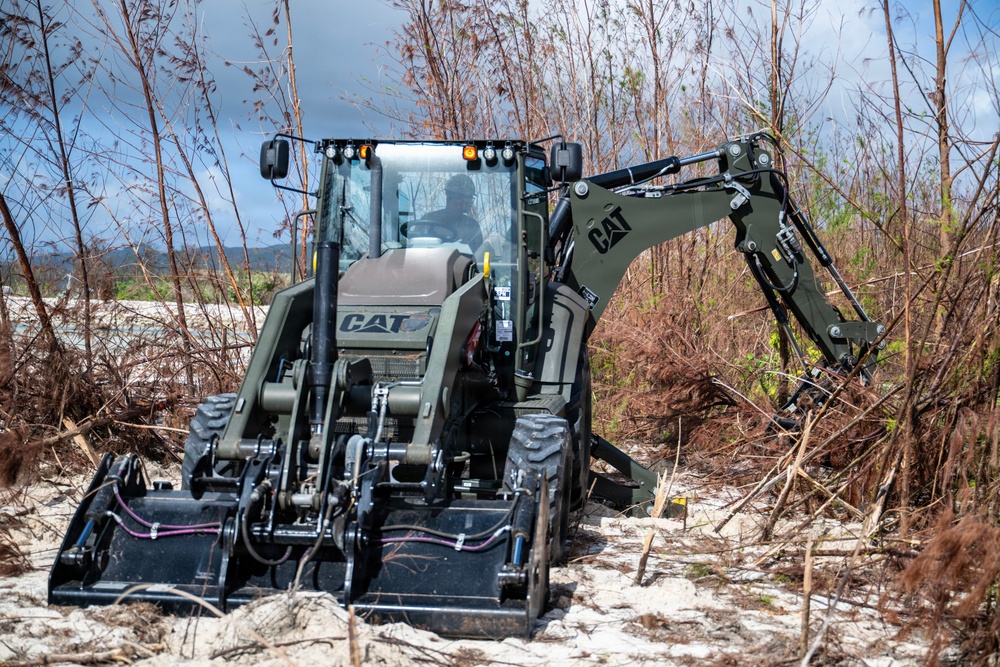 NMCB 1 Sailors clear an area with chainsaws and a backhoe
