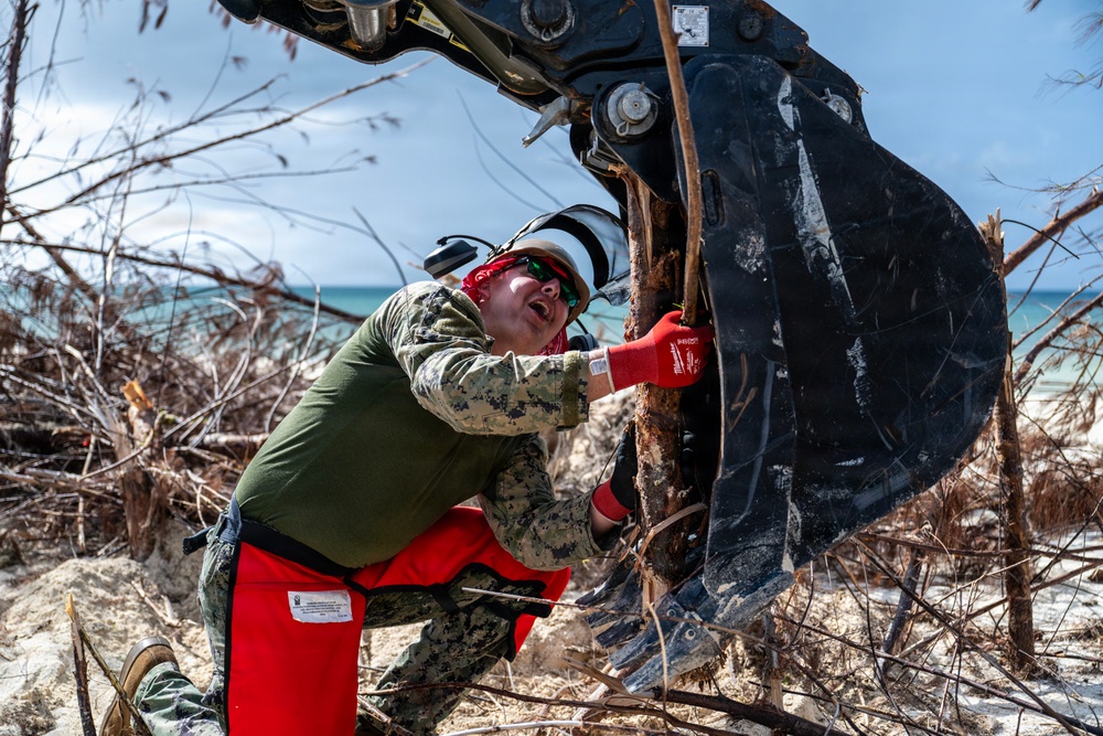 NMCB 1 Sailors clear an area with chainsaws and a backhoe