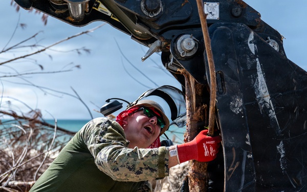 NMCB 1 Sailors clear an area with chainsaws and a backhoe