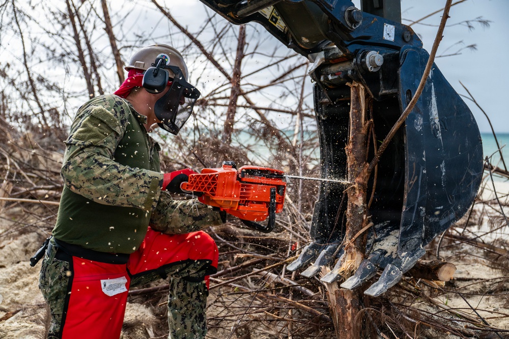 NMCB 1 Sailors clear an area with chainsaws and a backhoe