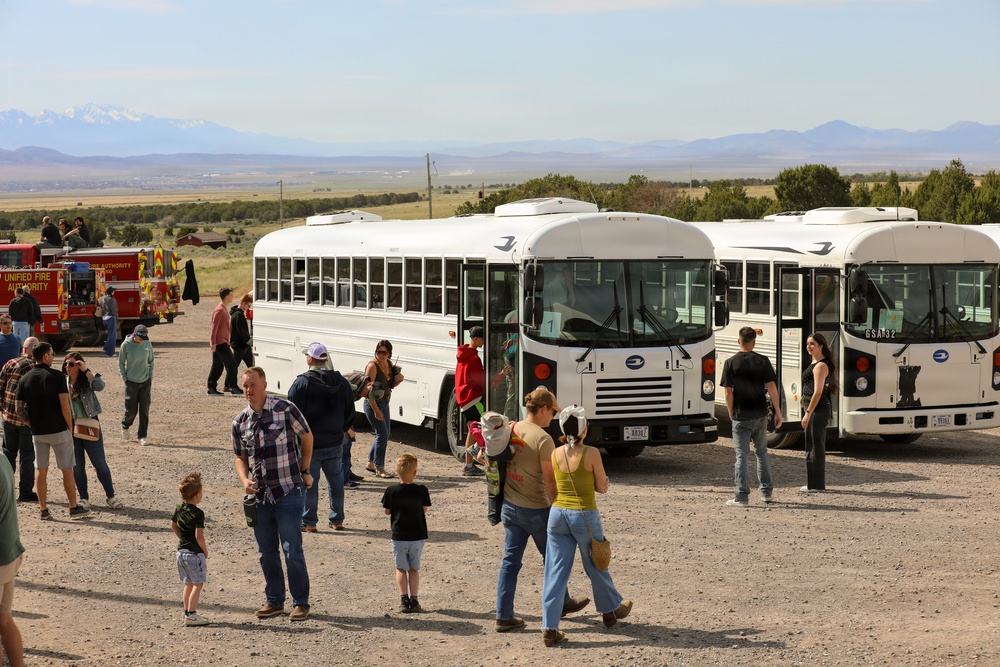 Visitors board white shuttle buses at a military installation open house event in a high desert setting