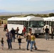 Visitors board white shuttle buses at a military installation open house event in a high desert setting