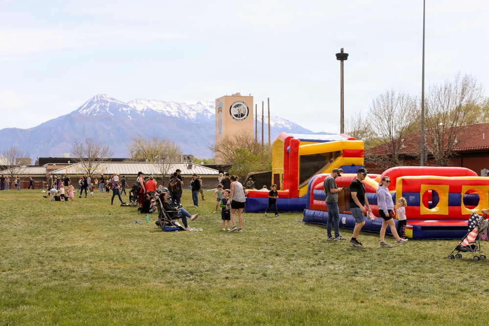 Military families gather for outdoor community event featuring inflatable bounce houses with snow-capped mountains in background