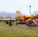 Military families gather for outdoor community event featuring inflatable bounce houses with snow-capped mountains in background