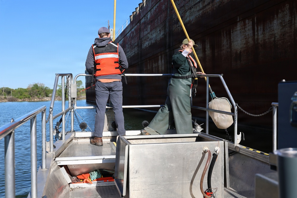 Two crew members working bow near large vessel hull