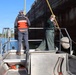 Two crew members working bow near large vessel hull