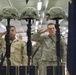 This image depicts a military memorial ceremony, commonly known as a 'Fallen Soldier Battle Cross' or 'Battle Cross Ceremony.' Three rifles are planted bayonet-down with combat helmets placed on top, serving as a traditional tribute to fallen soldiers. U.S. Army personnel in various uniforms are rendering salutes in honor of the deceased.