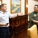 Two military personnel are engaged in conversation in what appears to be a formal meeting room or officers' lounge. One individual wears a light blue U.S. Air Force dress uniform with a major's rank insignia, while the other wears an olive green flight suit with patches indicating affiliation with the Philippines Navy. The setting suggests an official bilateral or diplomatic military meeting.