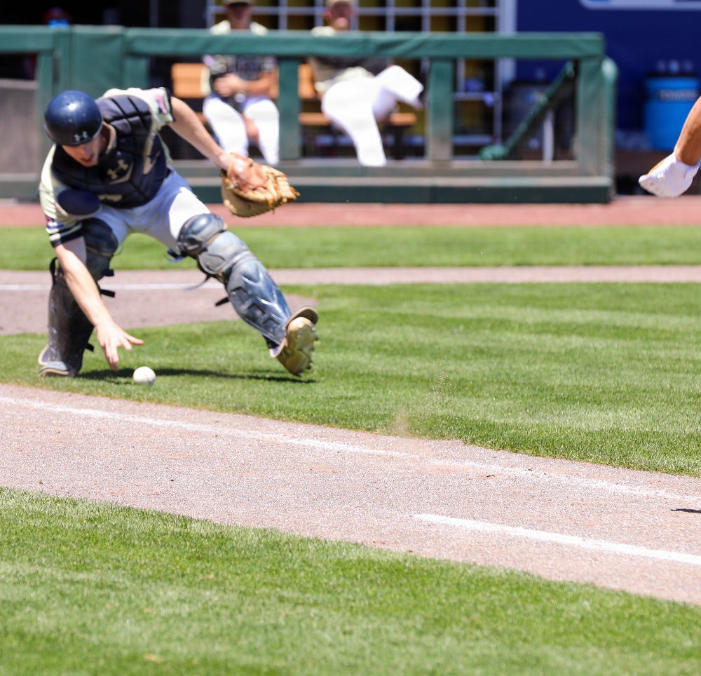 Baseball catcher scrambles to field a wild pitch near the first base line during a collegiate game