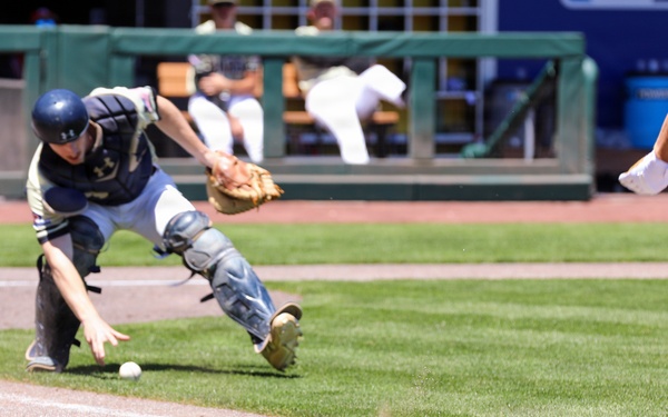 Baseball catcher scrambles to field a wild pitch near the first base line during a collegiate game