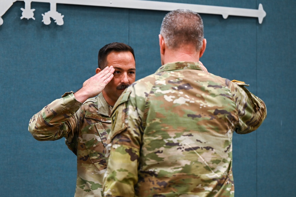 Two military personnel in U.S. Army Operational Camouflage Pattern (OCP) uniforms are engaged in a formal salute exchange. The soldier facing the camera, whose name tape reads 'RANCICO' (or similar), is rendering a salute to a senior soldier whose back is to the camera. This appears to be a formal military ceremony, possibly a promotion, award, or change of command event.