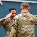 Two military personnel in U.S. Army Operational Camouflage Pattern (OCP) uniforms are engaged in a formal salute exchange. The soldier facing the camera, whose name tape reads 'RANCICO' (or similar), is rendering a salute to a senior soldier whose back is to the camera. This appears to be a formal military ceremony, possibly a promotion, award, or change of command event.