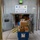 The image shows the Military Postal Service facility at Camp Bondsteel, with an APO AE 09240 address designation. Personnel are actively handling and moving packages and mail at the facility entrance. A soldier in camouflage uniform and a civilian worker are managing a large stack of cardboard boxes alongside blue USPS mail containers.