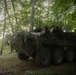 Camouflaged US Army Stryker armored vehicle concealed in wooded treeline during Spectrum Blitz 26