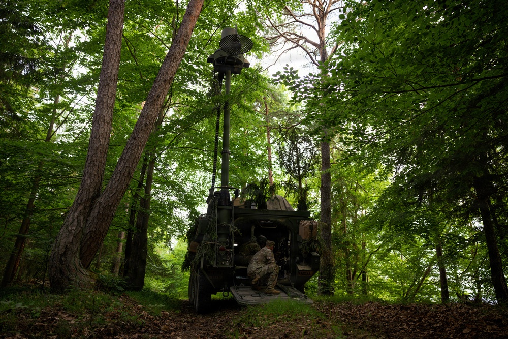 Soldiers operate military communications vehicle concealed in forest during Spectrum Blitz 26