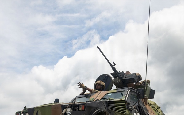 A French Army VBL (Véhicule Blindé Léger) light armored reconnaissance vehicle, serial number 69840046, is photographed on a gravel surface during what appears to be a military exercise or training event. The vehicle bears the number '4' on the front and '22' on the side, and is equipped with a roof-mounted machine gun and a radio antenna. At least one crew member is visible in the open hatch, raising a hand.