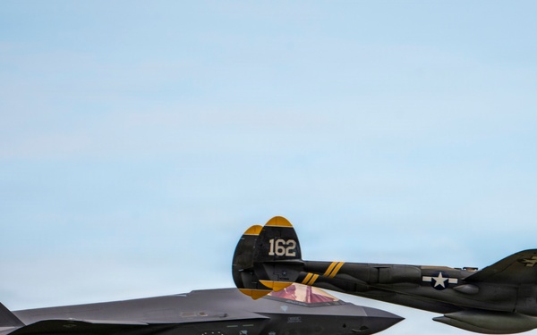 Two military aircraft are flying in formation against a partly cloudy sky. The formation pairs a modern F-35 Lightning II stealth fighter jet with a World War II-era propeller-driven aircraft, likely a P-38 Lightning or similar twin-boom design. This appears to be an airshow heritage flight demonstrating the evolution of American air power.
