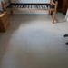 A sparse, minimally furnished room with a tile floor, featuring a bed frame without a mattress, a wooden nightstand, and a blue office chair. The room appears to be in a transitional state, possibly a dormitory or budget accommodation being set up or cleared out. Notable is the absence of bedding or a mattress on the slatted bed frame.