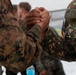 Two military personnel from different nations are clasping hands in a firm handshake or greeting gesture. One soldier wears US Marine Corps MARPAT woodland camouflage, while the other wears a different digital camouflage pattern with a name tape reading 'TAMBALO' and what appears to be a Philippine flag patch. The image likely depicts a bilateral military exercise or cooperative engagement between US and Philippine armed forces.