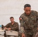 A Philippine Navy servicemember named Tamayao, wearing digital camouflage uniform with a Philippine flag patch, is leaning over a table and reviewing printed materials inside a military tent. In the background, at least two US Marines in MARPAT uniforms are seated at folding tables, appearing to take notes. The setting suggests a joint military briefing or training exercise.