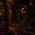 Military personnel are working inside what appears to be the cargo hold of a military transport aircraft, handling heavy chains and tie-down equipment. The scene is dimly lit with warm amber tones, showing at least two service members in military attire securing or unsecuring cargo restraint chains. Red equipment or gear is visible on the floor in the background.