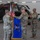 Task Force Vipers transfer authority to Task Force Gunfighters U.S. Army soldiers in OCP (Operational Camouflage Pattern) uniforms are conducting a military ceremony, likely a casing or uncasing of colors, inside a helicopter hangar. Three soldiers are handling a blue unit guidon/flag featuring an eagle emblem with gold fringe, while two additional soldiers stand at attention nearby. The setting includes a military helicopter (appears to be an AH-64 Apache) in the background along with American and unit flags.