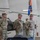 Task Force Vipers transfer authority to Task Force Gunfighters A military ceremony taking place inside an aircraft hangar, featuring U.S. Army soldiers in OCP (Operational Camouflage Pattern) uniforms standing at parade rest. An AH-64 Apache attack helicopter is visible in the background, along with U.S. and Polish flags, suggesting this may be taking place at a joint base in Poland. The formal arrangement of personnel and presence of a unit guidon flag indicate this is likely a change of command or activation ceremony.