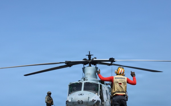 A U.S. Sailor signals a UH-1Y Venom helicopter, assigned to Marine Medium Tiltrotor Squadron (VMM) 365 (Reinforced), Littoral Combat Force 24.