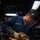 Hull Technicians Aboard USS Boxer Perform Welding, Grinding A U.S. Navy sailor named Hemelgarn is using an angle grinder on a metal surface in what appears to be a shipboard workshop or machine shop. Bright orange sparks are flying dramatically from the grinding operation. The sailor is wearing appropriate personal protective equipment including a face shield, safety glasses, ear protection, and heavy-duty work gloves.