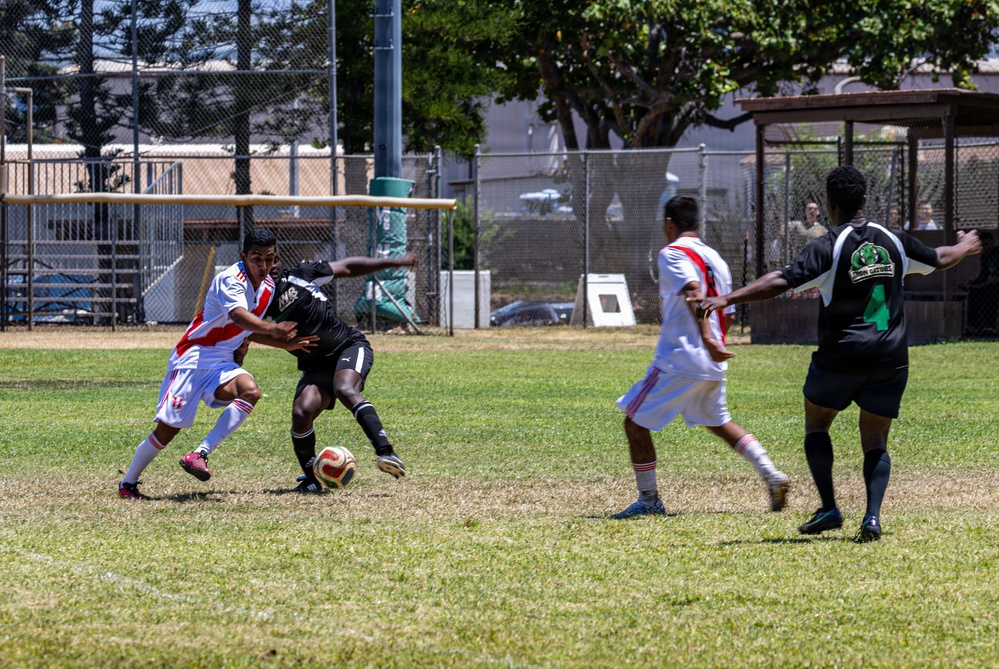 A soccer match is being played on a grass field, with players from two teams competing for the ball. One team wears white jerseys with red stripes, while the other wears black uniforms. The action is centered around a contested ball possession near the middle of the field.