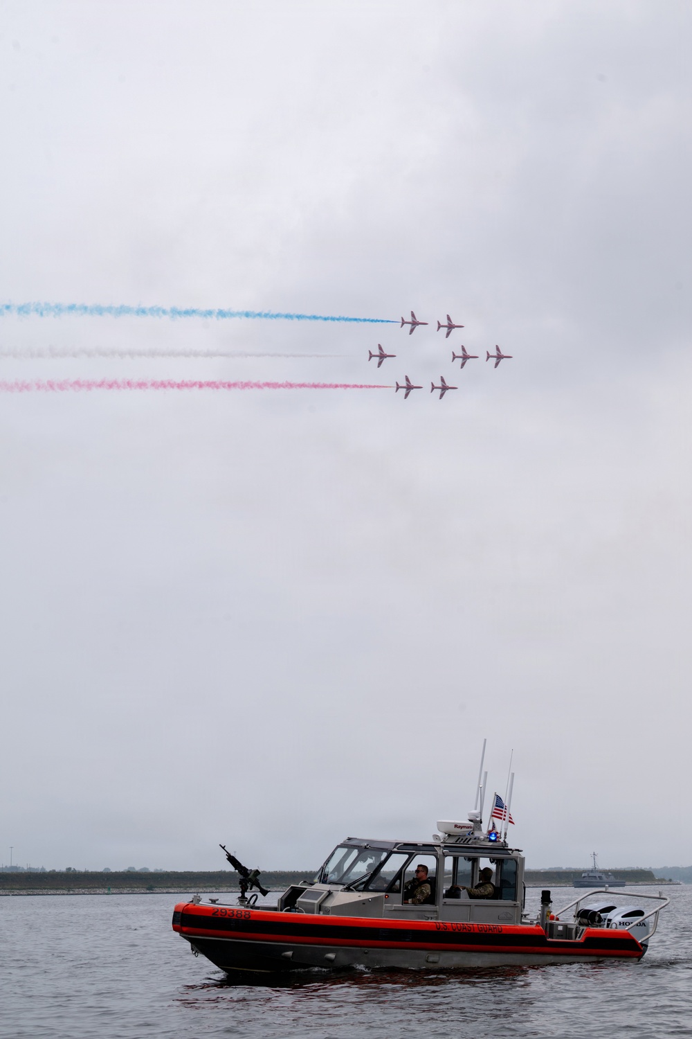 Royal Air Force Red Arrows perform over waterway as U.S. Coast Guard vessel patrols below