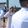 USS South Dakota (SSN 790) Holds Change of Command Ceremony A formal military ceremony is taking place at a naval installation, with uniformed U.S. Navy personnel rendering salutes. At least three individuals in white dress uniforms are visible, including an officer wearing a combination cover with gold oak leaf insignia and service ribbons. The setting appears to be a pier or waterfront facility with naval vessels and cranes visible in the background.