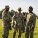 Three U.S. Army soldiers in Operational Camouflage Pattern (OCP) uniforms are standing on a grass field engaged in conversation. Two of the soldiers are wearing Drill Sergeant campaign hats, indicating their role as Drill Sergeants. The setting appears to be an outdoor military or community event during daytime.