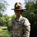 A U.S. Army Staff Sergeant named Jones stands at ease in an outdoor setting wearing the OCP (Operational Camouflage Pattern) uniform and a Drill Sergeant campaign hat. The soldier displays rank insignia consistent with Staff Sergeant (E-6) and wears unit patches on the left sleeve. The image appears to be an official or semi-official portrait taken in a grassy, tree-lined environment.