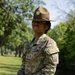 A U.S. Army Drill Sergeant stands outdoors in a grassy, tree-lined area wearing the distinctive campaign (Smokey Bear) hat and OCP (Operational Camouflage Pattern) uniform. The name tape reads 'JONES' and the rank insignia indicates Staff Sergeant. A unit patch is visible on the right sleeve.