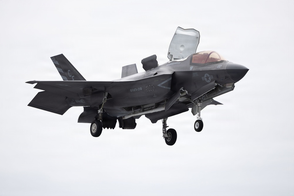 A U.S. Marines F-35B Lightning II stealth fighter jet is captured in flight with landing gear deployed and the lift fan door open on top of the fuselage, indicating a short takeoff or vertical landing (STOVL) configuration. The aircraft bears U.S. Marine Corps markings and is photographed against an overcast sky. The tail code and fuselage markings suggest it belongs to a Marine Fighter Attack Training Squadron.