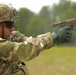 A U.S. Army soldier in MultiCam (OCP) uniform and ACH helmet is aiming a pistol in a two-handed grip at a firing range. The soldier is wearing tactical gloves, ballistic eyewear, and has a name tape reading 'SAGER' visible on the helmet. The firearm appears to be a SIG Sauer M17/M18 pistol, the U.S. Army's current standard-issue sidearm, identifiable by its coyote tan finish.