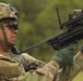A U.S. Army soldier identified by the name tape 'SAGER' is handling what appears to be an XM25 Counter Defilade Target Engagement (CDTE) system or similar grenade launcher with an advanced optic/targeting system mounted on top. The soldier is wearing OCP (Operational Camouflage Pattern) uniform, tactical gloves, ballistic eyewear, and an ACH helmet with a device mounted on it. The image appears to be taken during a training or demonstration event in an outdoor setting.
